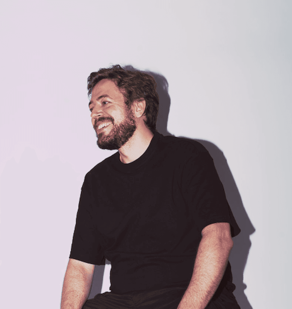 Portrait of Šimon Leška laughing, sitting against a light wall